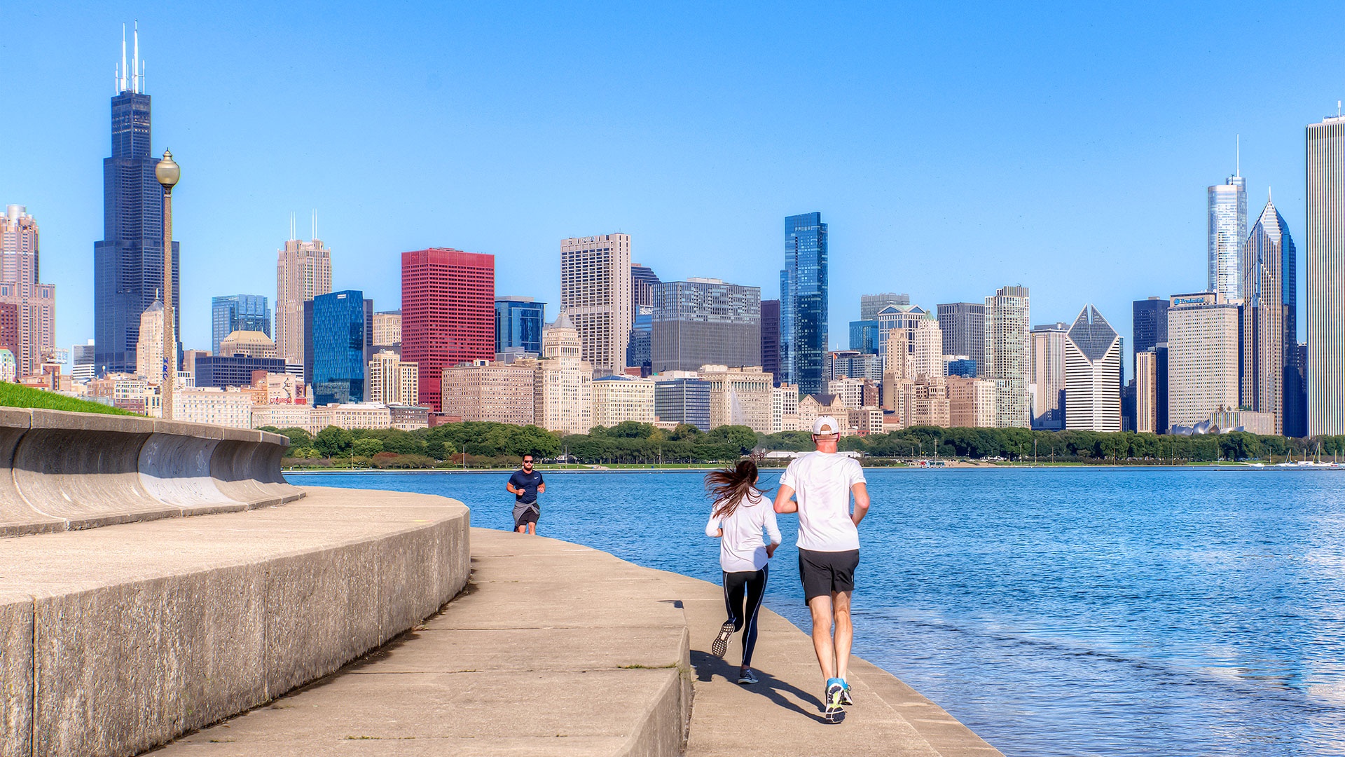 A couple jogs along the Adler Planetarium Skyline Walk. Lake Michigan is on their right and the Chicago skyline is seen in the background.